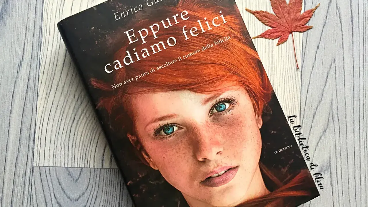 Copertina del libro "Eppure cadiamo felici" di Enrico Galiano, con il volto di una ragazza dai capelli rossi e occhi azzurri. Una foglia d'acero rossa completa la scena.