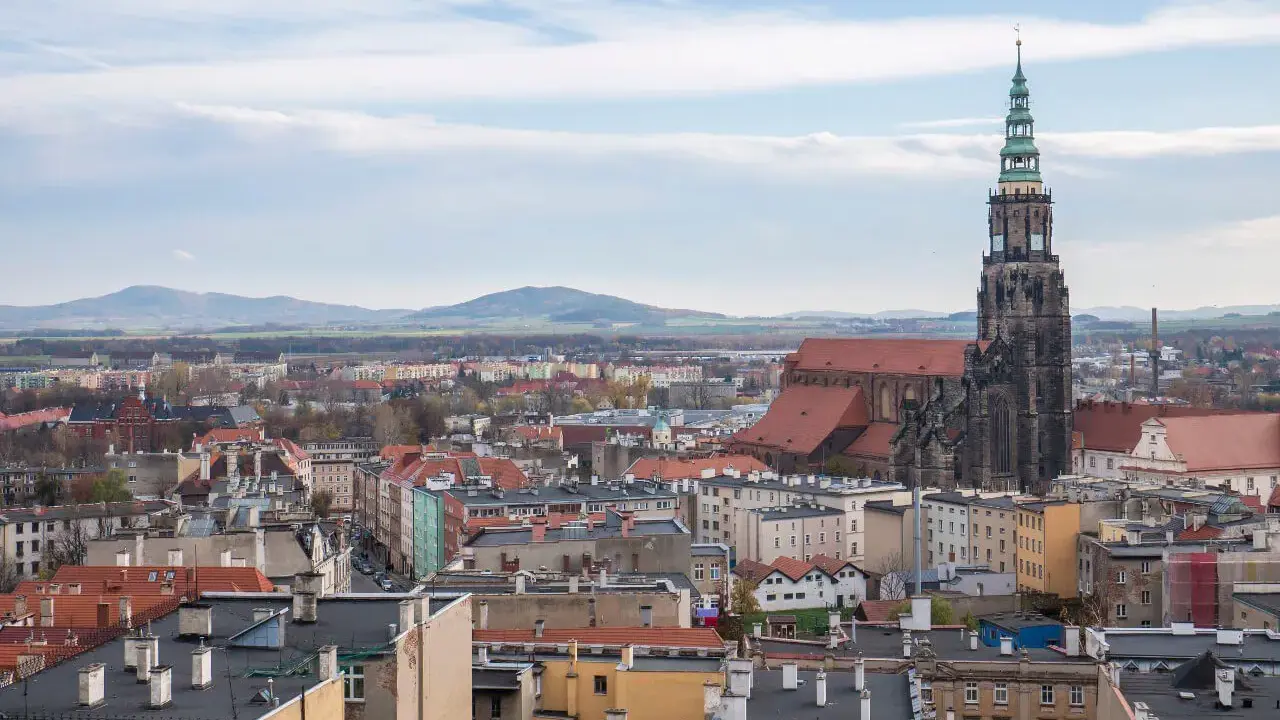Widok na miasto z dominującą wieżą katedry. W oddali góry. Odkryj **Świdnica atrakcje**!