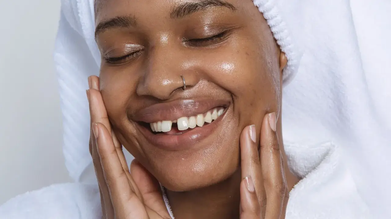Visage radieux d'une femme souriante, peau hydratée après l'utilisation de rétinol. Elle porte une serviette sur la tête et un peignoir blanc.