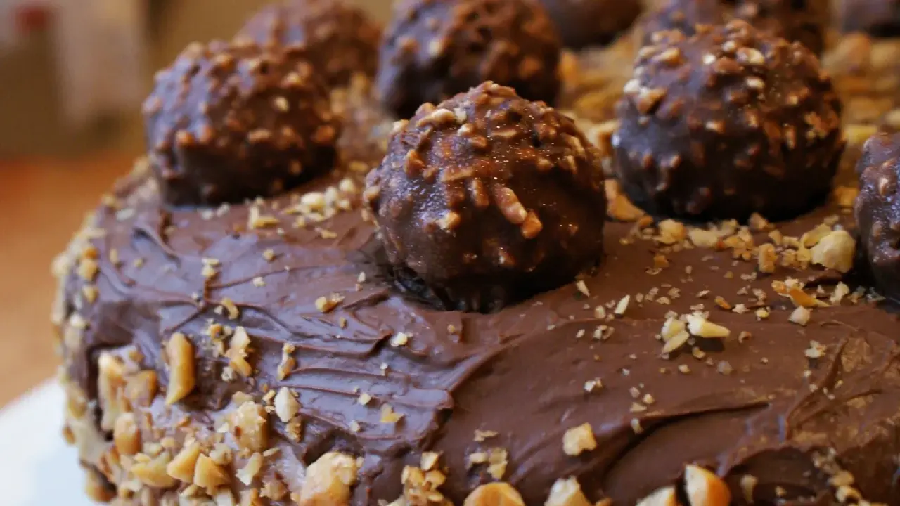 Pyszny tort ferrero rocher, obficie udekorowany czekoladowymi kulkami i posypany orzechami.