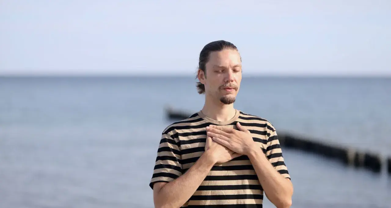 Mann mit geschlossenen Augen und Händen auf der Brust, genießt die frische Meeresluft. Eine asthma kur am meer kann Wunder wirken.