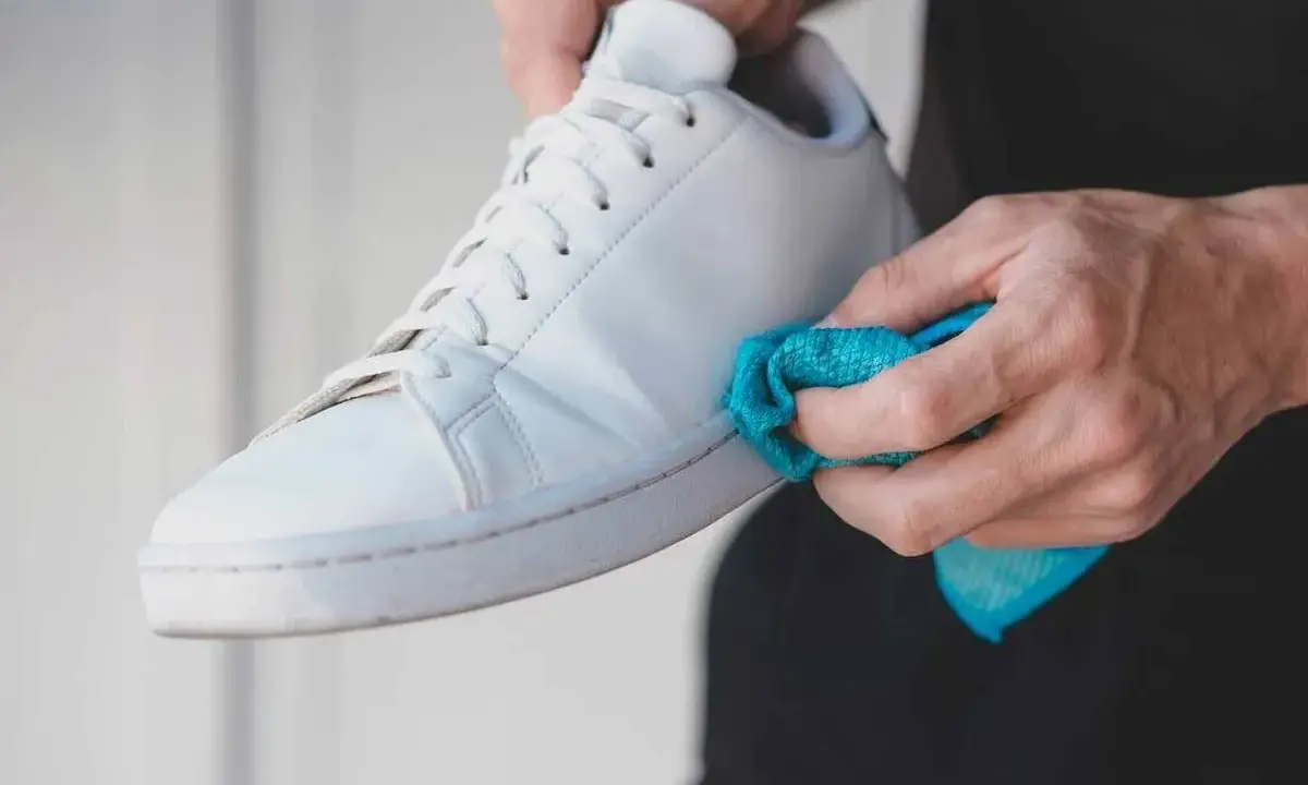 Manos limpiando zapatillas blancas de tela con un paño azul.