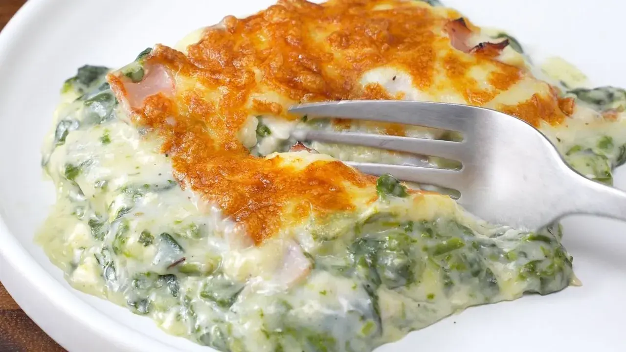 Deliciosa lasaña de espinacas cremosa, gratinada y lista para disfrutar. Un tenedor se hunde en esta maravilla.
