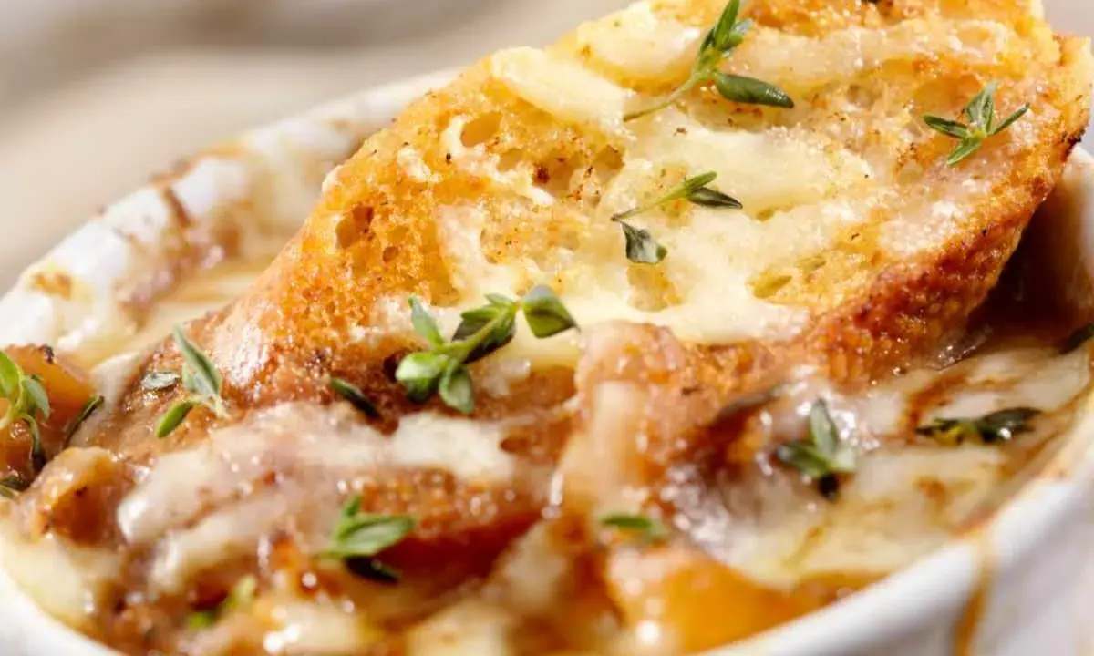 Una ricca zuppa di cipolle toscana, con crostini dorati e formaggio fuso, guarnita con timo fresco.