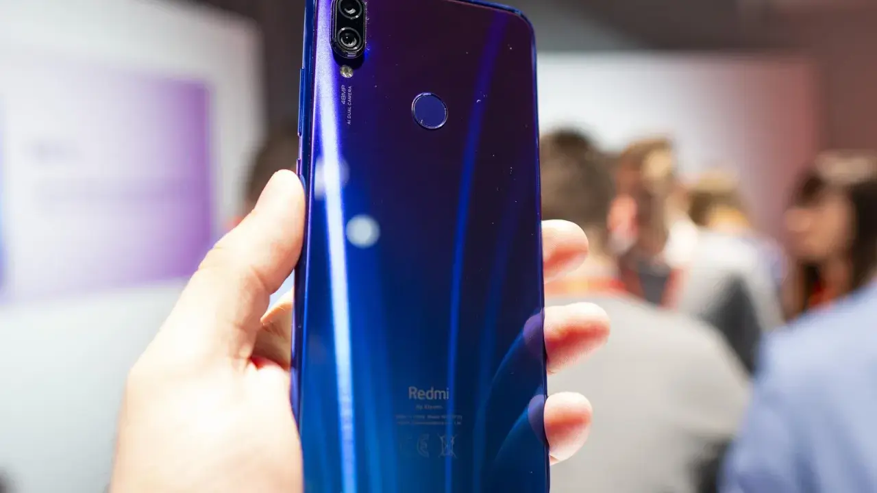 Błyszczący, niebieski tył telefonu Redmi 7 Pro z podwójnym aparatem 48MP i czytnikiem linii papilarnych, trzymany w dłoni.