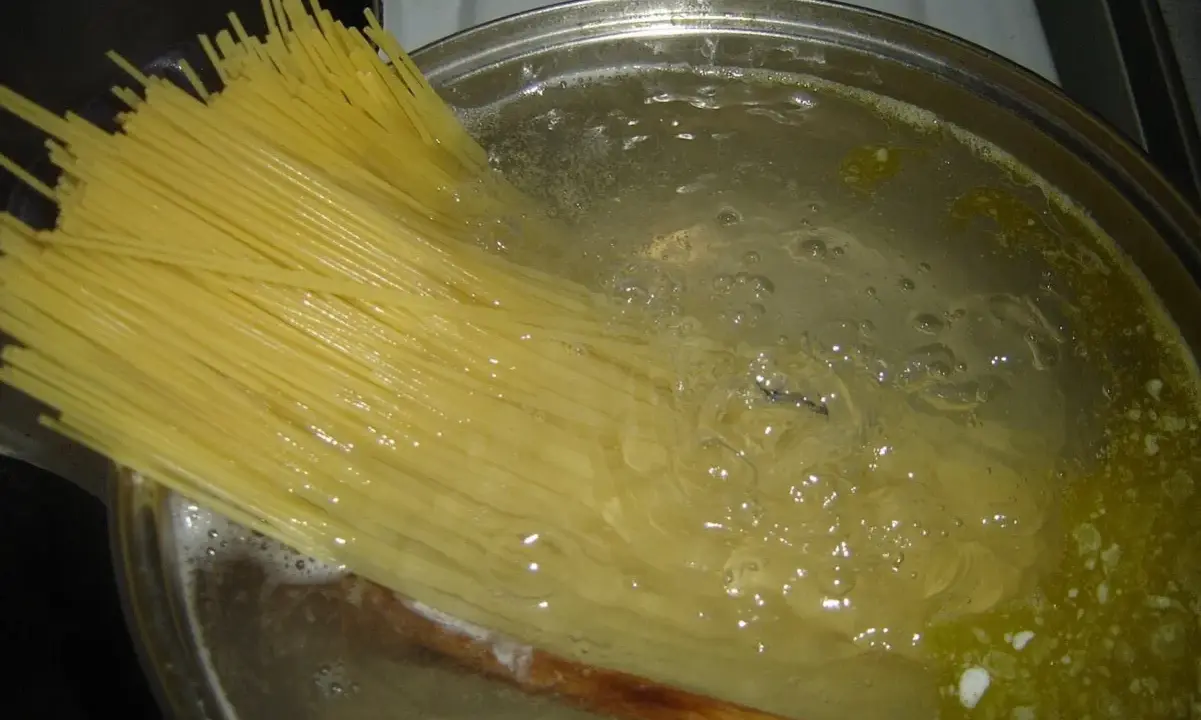 Długi makaron spaghetti zanurza się w gotującej wodzie. Czas, ile gotuje się makaron, zależy od jego grubości.