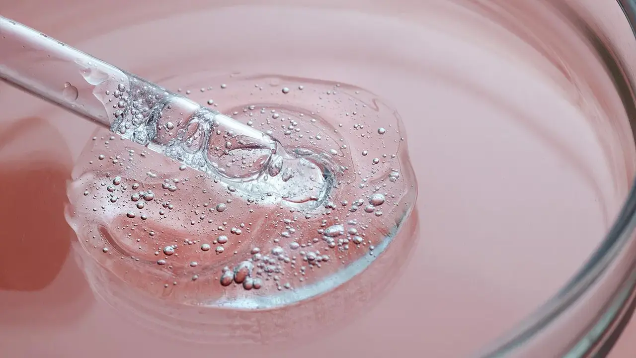 Goccia di siero trasparente con bollicine, su sfondo rosa. Un tocco di vitamina B3 per il viso.