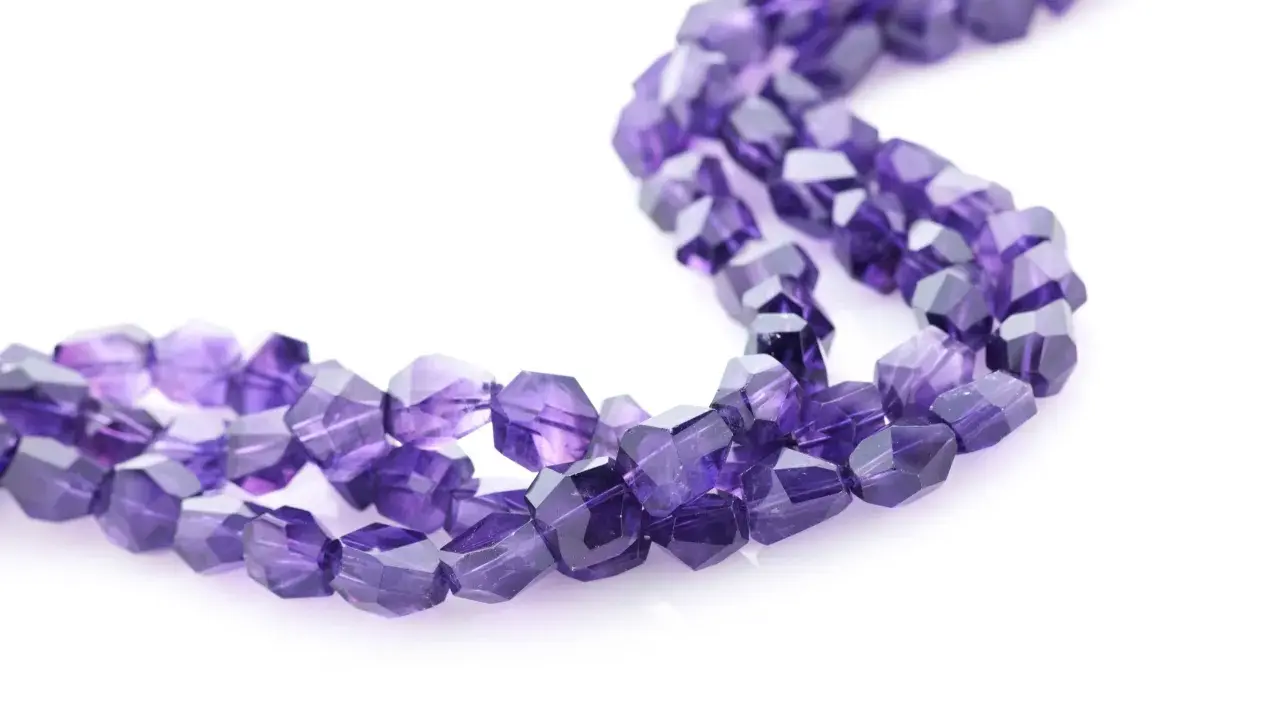 Tre fili di sfaccettate pietre viola, il cui nome è ametista, su sfondo bianco.