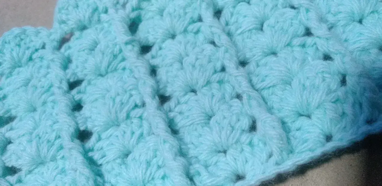 Textura de un tejido a crochet en tono azul claro. Se aprecian los detalles de un punto fantasía, creando un patrón con relieve y pequeños huecos.