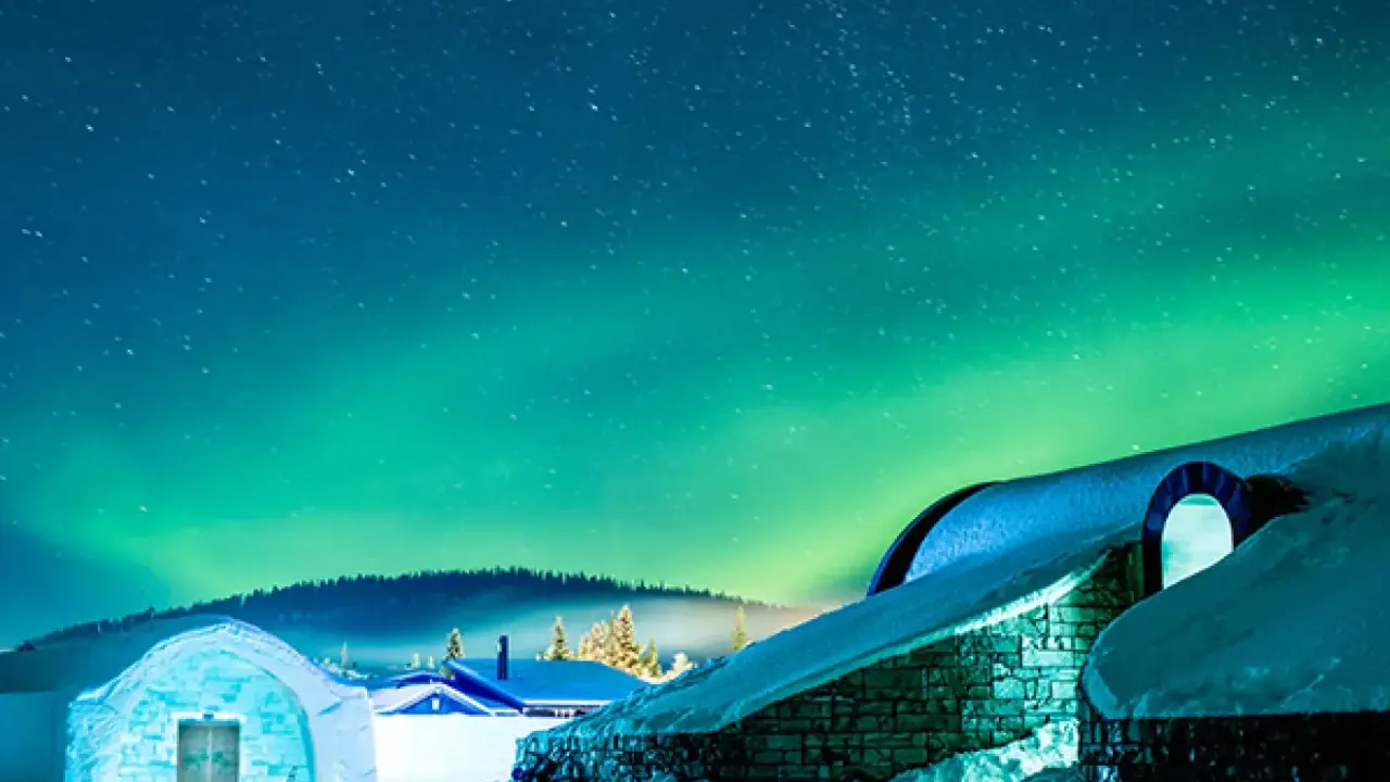 Snöklädda byggnader under norrsken. En magisk plats att se norrsken i Sverige.