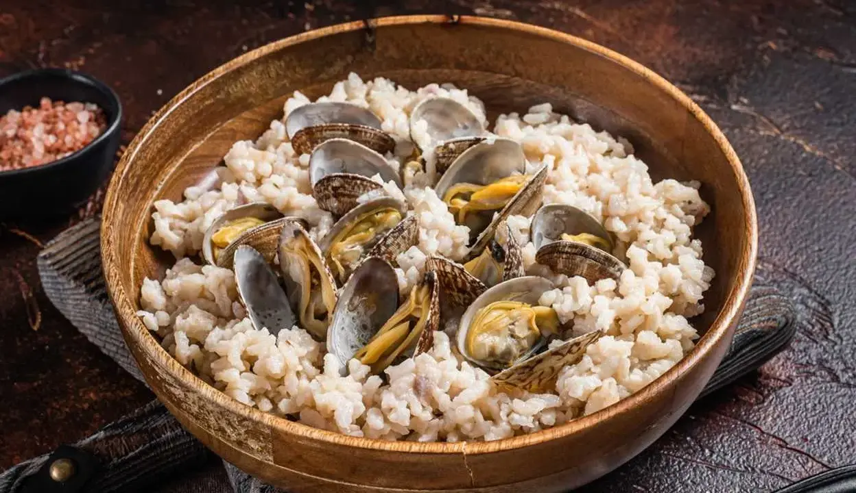Un delicioso arroz con almejas, servido en un cuenco de madera. Las almejas, abiertas y jugosas, se mezclan con el arroz cremoso.