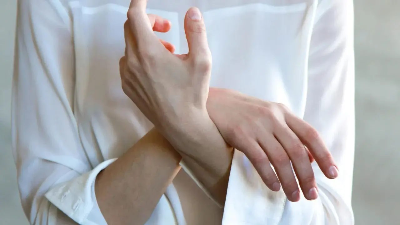 Frau hält sich das Handgelenk, als ob sie einen stechenden Schmerz im Handgelenk bei Drehbewegung spürt.