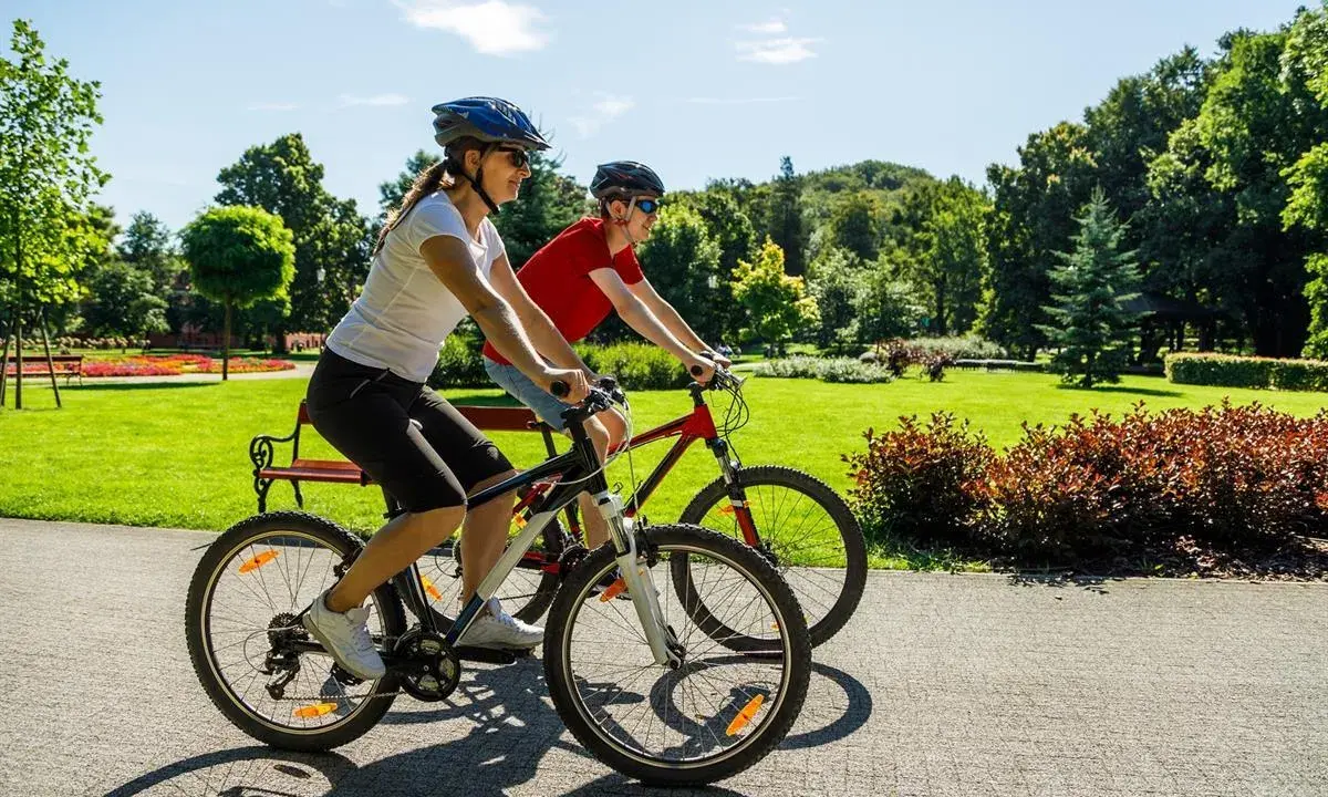 Dwie osoby na rowerach cieszą się piękną pogodą w parku. To pokazuje, co daje jazda na rowerze: aktywność, relaks i kontakt z naturą.