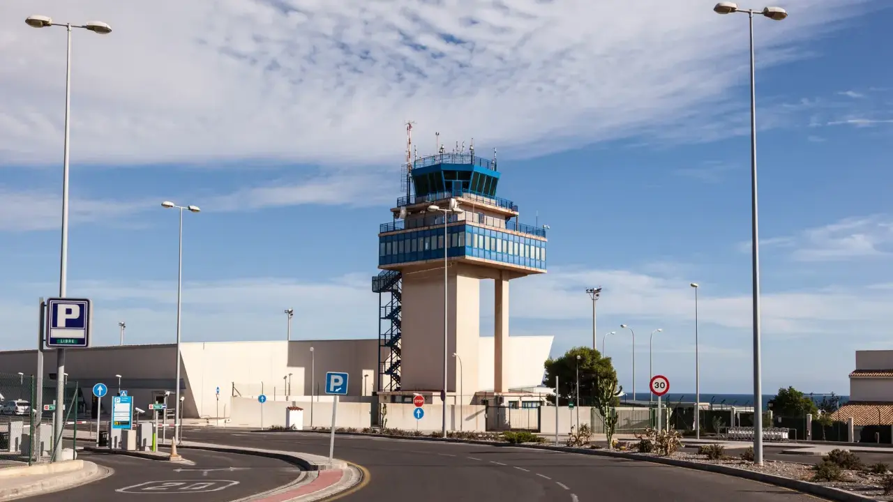 Kontrollturm am Almeria Airport mit Parkplatzschildern und Straßenbeleuchtung unter blauem Himmel.