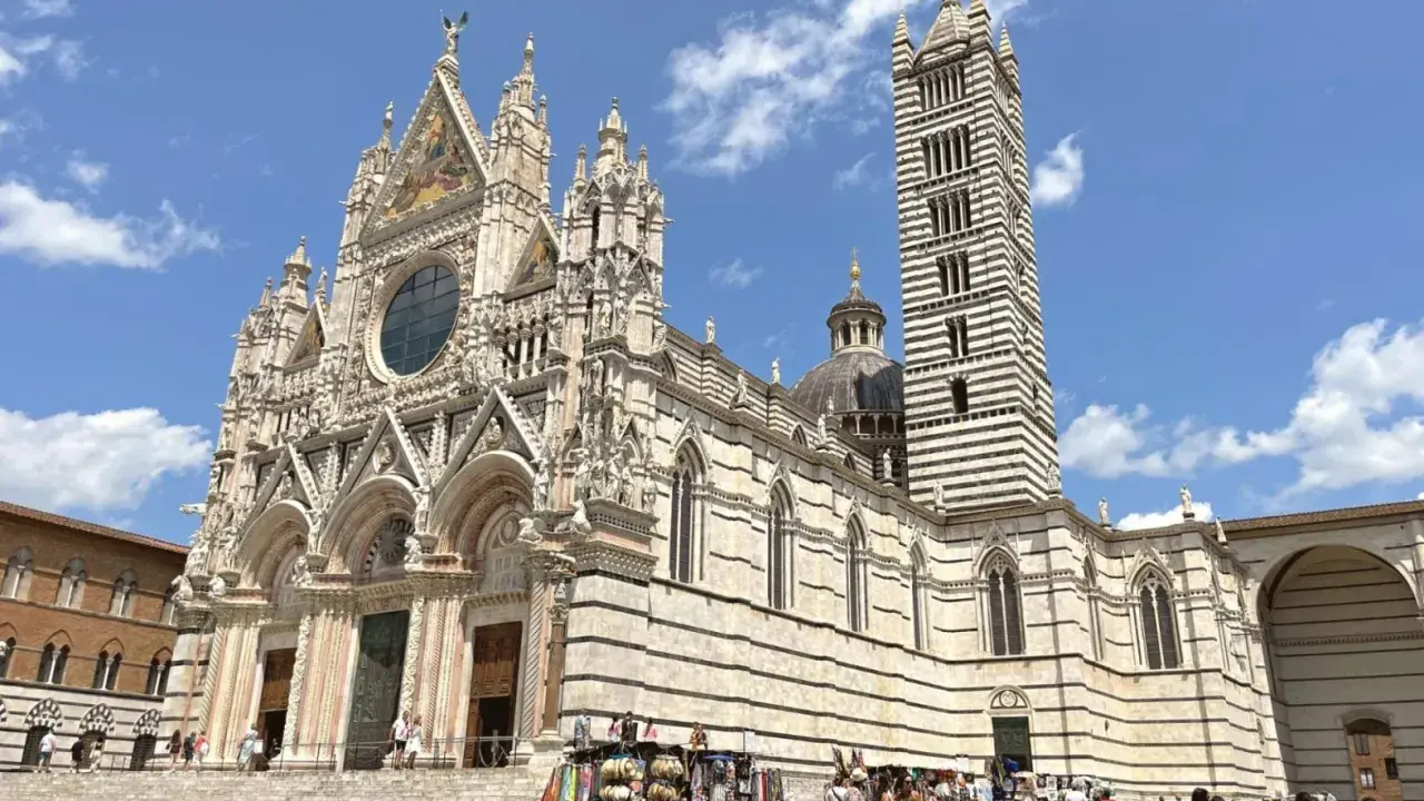 Il Duomo di Siena, con la sua imponente torre campanaria a strisce, è un must per chi cerca cosa visitare a Siena. La piazza antistante è animata da bancarelle.