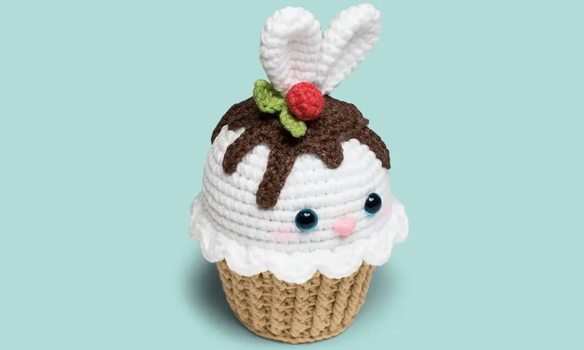 Adorable cupcake amigurumi con orejas de conejo, glaseado blanco, chispas de chocolate y una cereza. ¡Un dulce amigo tejido!