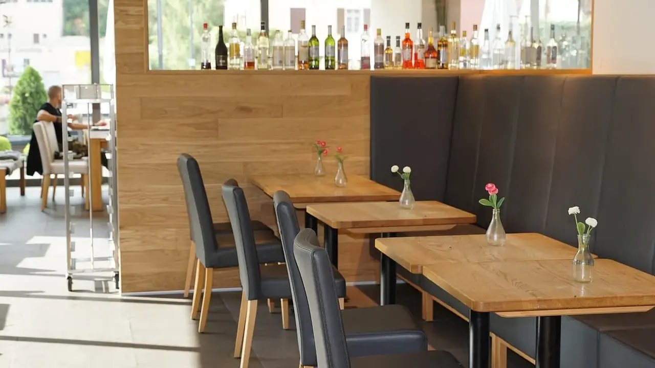 Mesas de madera con floreros y sillas negras en un restaurante. La distancia entre mesas permite un espacio cómodo.