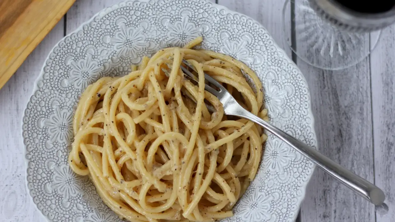 Porcja pysznego cacio e pepe na ozdobnym talerzu, z widelcem w makaronie.