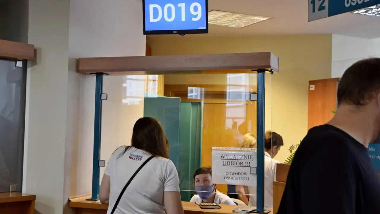 Kobieta czeka na odbiór dowodu rejestracyjnego. Na ekranie wyświetla się numer stanowiska D019.