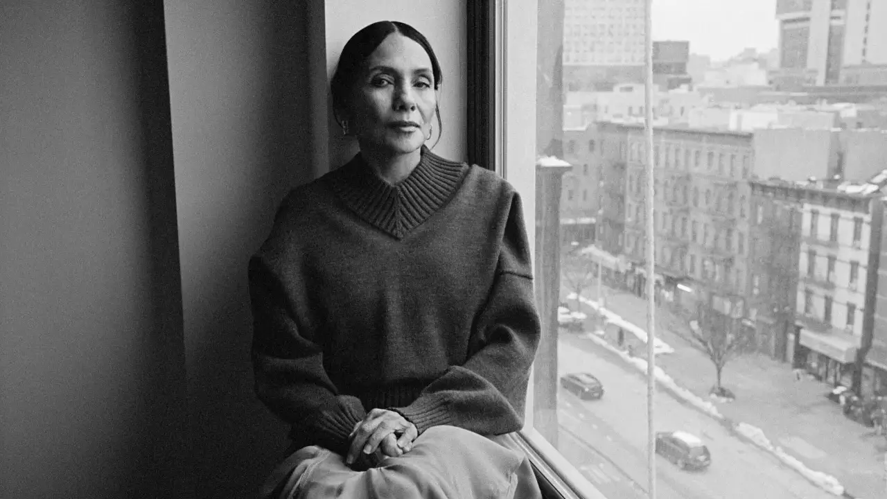 Ming Smith, a woman with her hair pulled back, sits by a window, looking out at a city street.