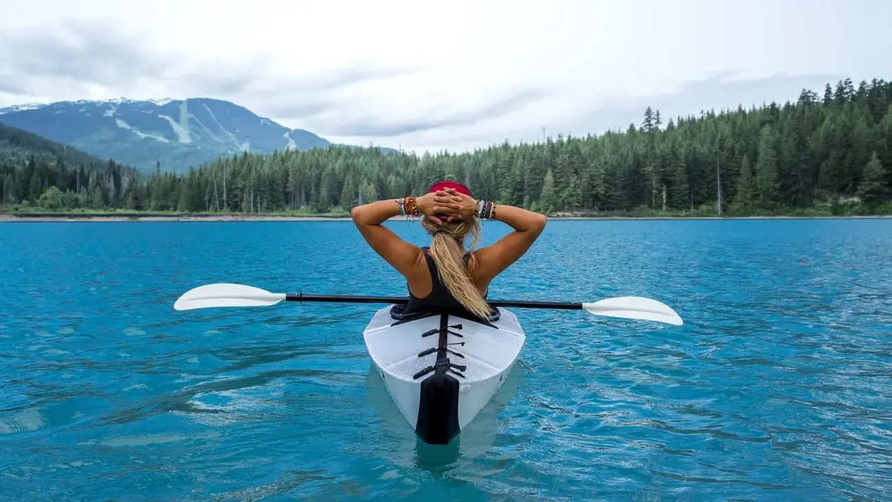 Kobieta w kajaku składanym relaksuje się na turkusowym jeziorze, otoczona lasem i górami.