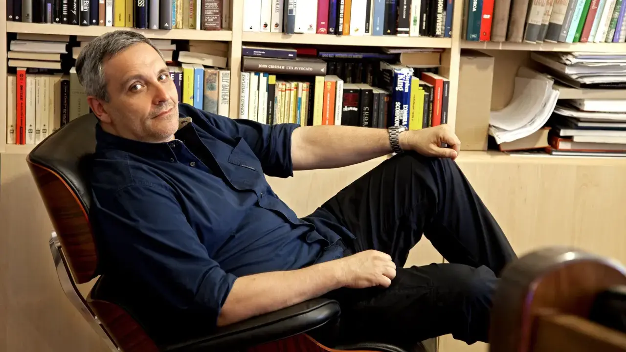 L'autore, circondato da libri, si rilassa su una poltrona. Tra i titoli, si intravede un riferimento a de Giovanni ultimo libro.