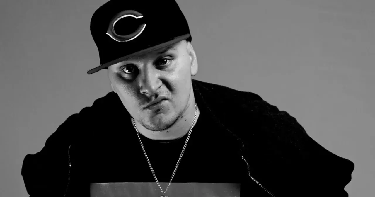 Mroczny ruby raper w czapce z daszkiem i łańcuchem, zamyślony.