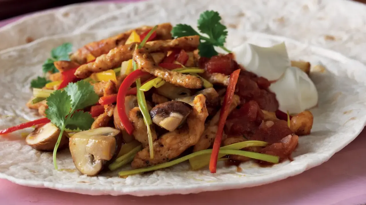 En läcker portion fajitas kyckling med paprika, champinjoner och gräddfil på en tortilla.