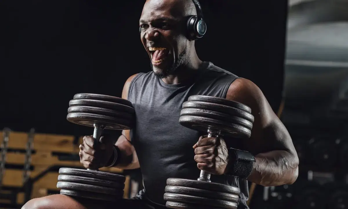 Uomo con cuffie nella palestra gym, solleva pesi con musica per allenamento. Grinta e determinazione.