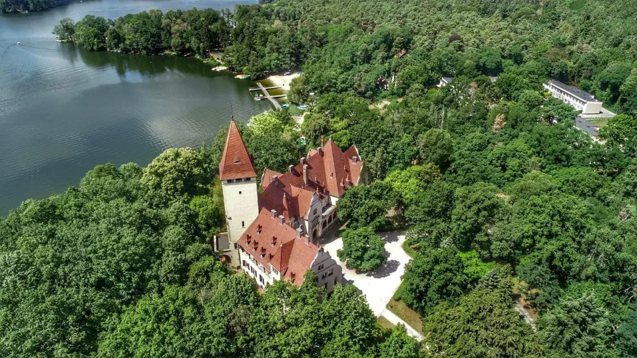 Zamek w Lubniewicach, otoczony bujną zielenią, malowniczo położony nad jeziorem.