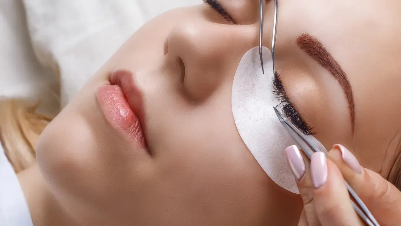 Une esthéticienne utilise des pinces pour appliquer des extensions de cils, une étape clé pour savoir comment coiffer ses sourcils et sublimer le regard.