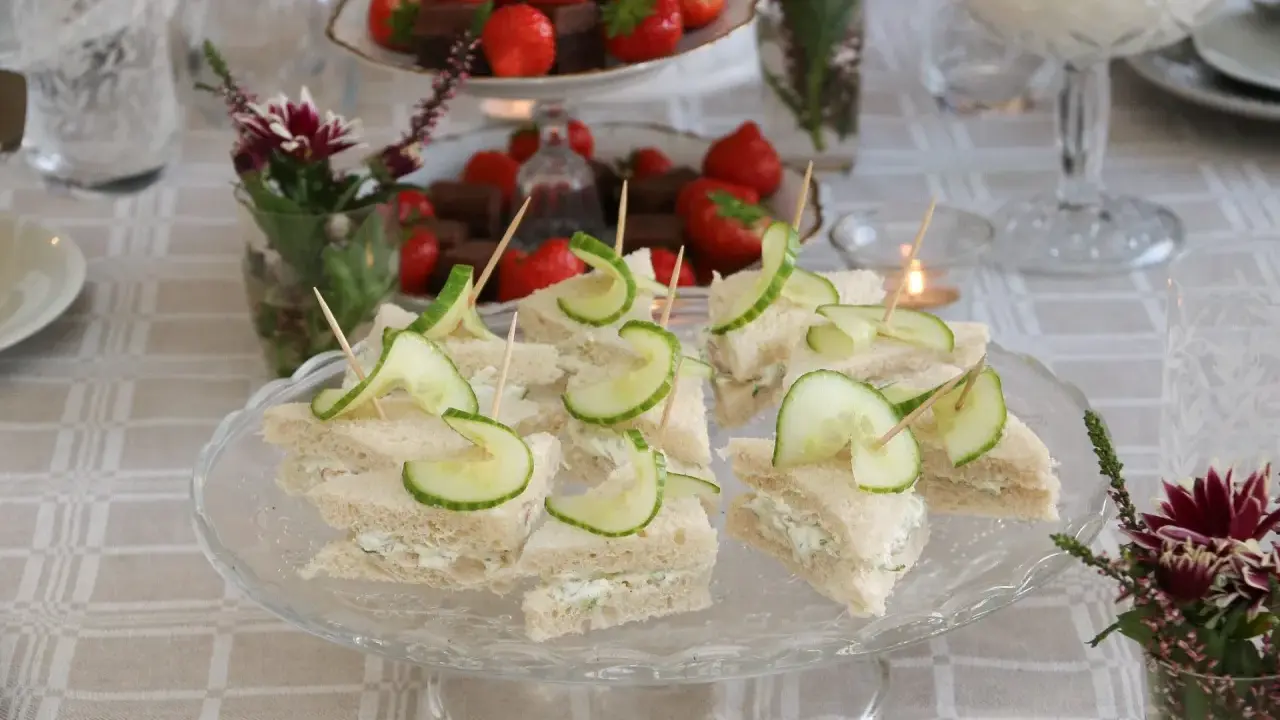 Smörgåsar med gurka och krämig fyllning, perfekta för ett afternoon tea recept. Jordgubbar och choklad i bakgrunden.