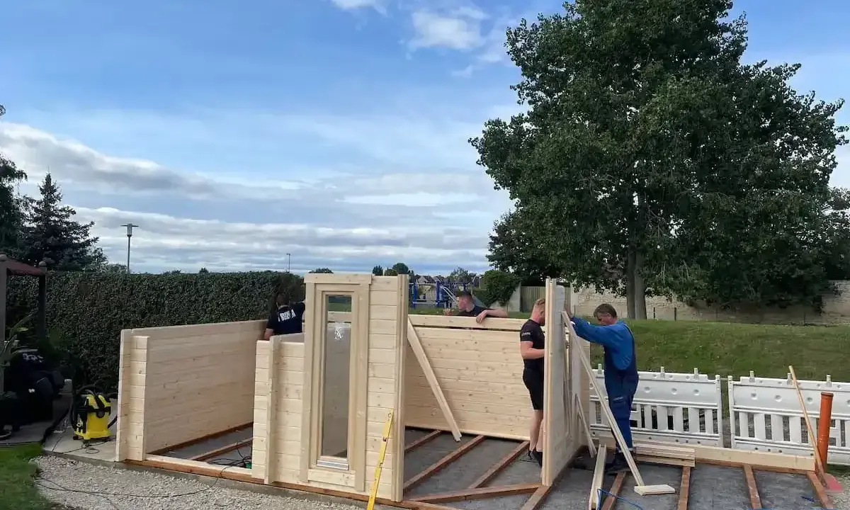 Männer bauen ein Gartenhaus. Die Montage schreitet voran, die Baugenehmigung ist hoffentlich vorhanden.
