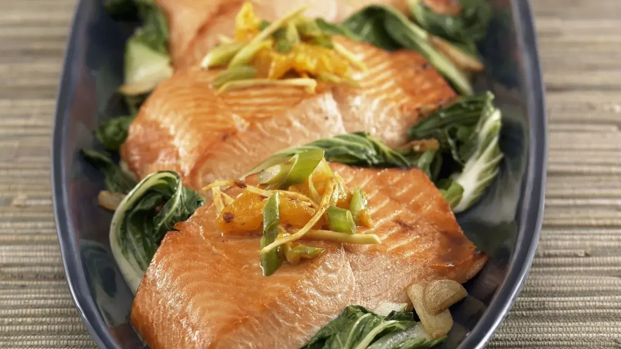 Saftiger Lachs mit Mangold, garniert mit Ingwer und Frühlingszwiebeln, auf einem dunkelblauen Teller serviert.