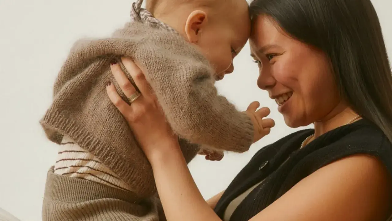 Madre y bebé se miran con ternura, frente con frente. El bebé, envuelto en un suéter de lana, muestra el apego infantil.
