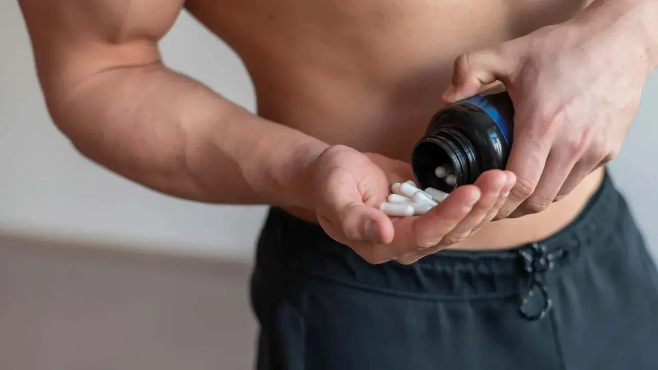 Muskulöser Mann nimmt Kapseln ein, um die BCAA Wirkung für den Muskelaufbau zu nutzen.
