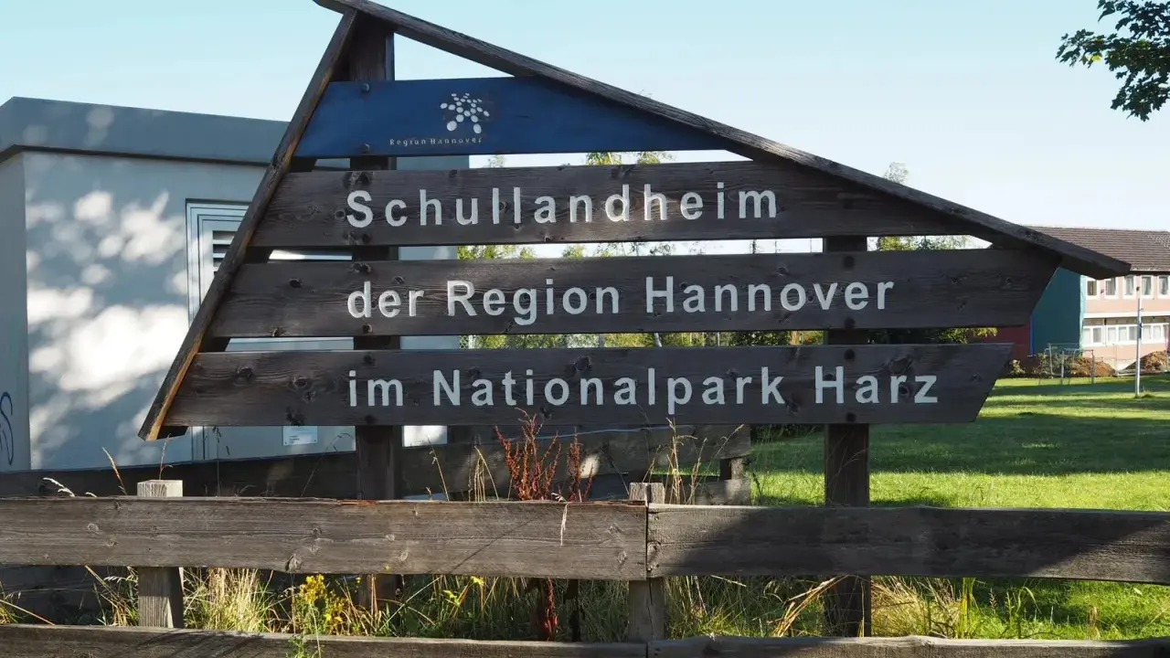 Drewniany drogowskaz "Schullandheim der Region Hannover im Nationalpark Harz" zapowiada przygodę w górach w Niemczech, być może z widokiem na szczyt Brocken.