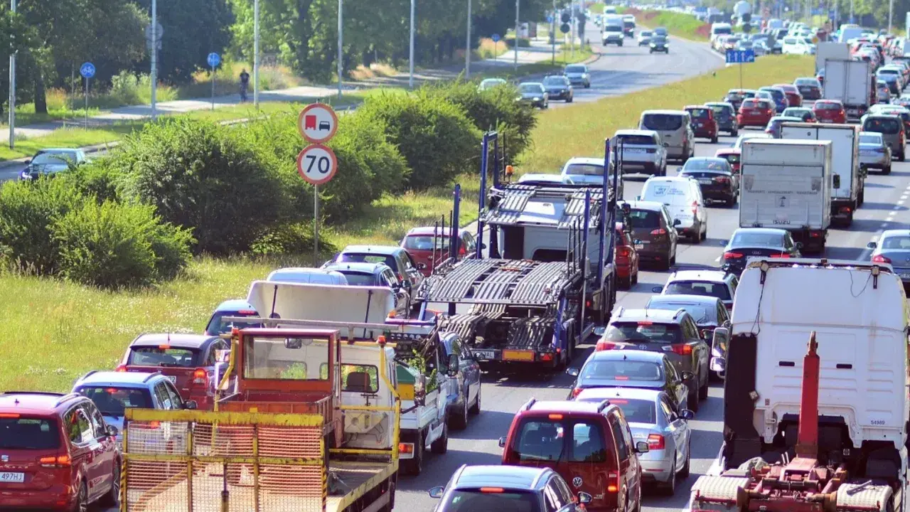 Korek na drodze, sznur samochodów i ciężarówek. Widać znak ograniczenia prędkości do 70. Może to być sytuacja wymagająca polisa car.