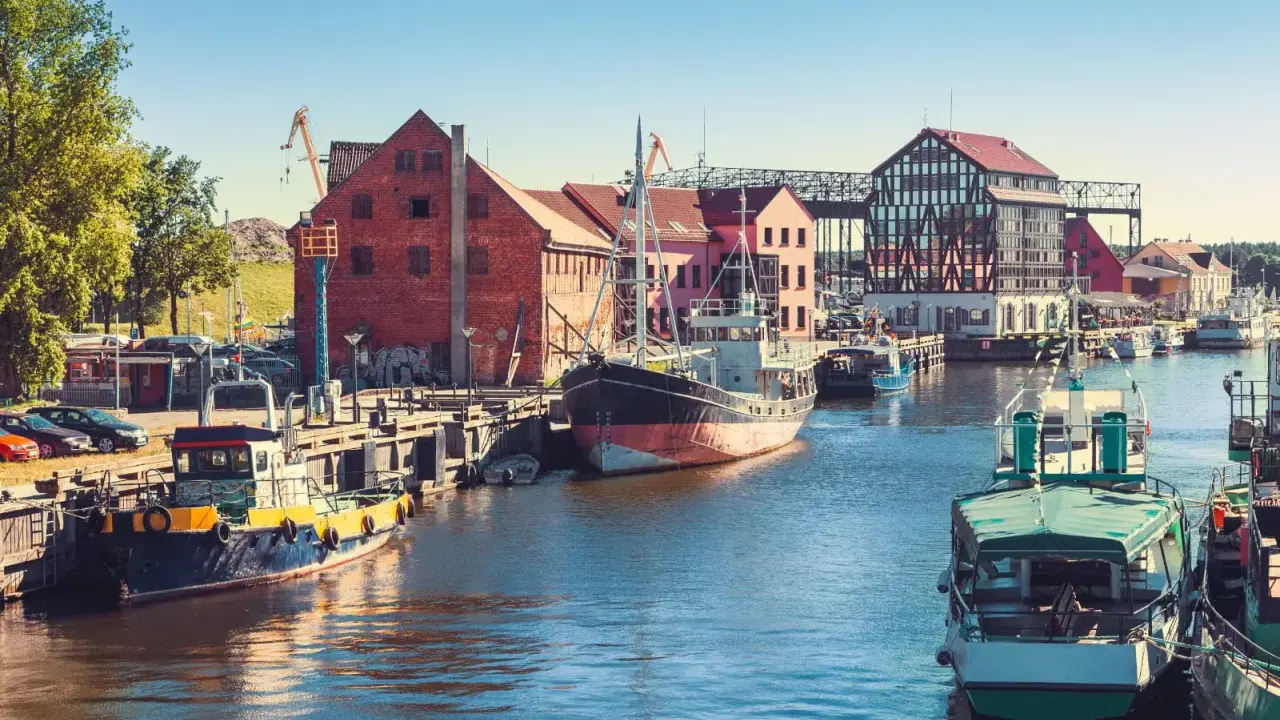 Barche ormeggiate nel porto di Klaipeda, Lituania, con edifici storici e gru sullo sfondo.