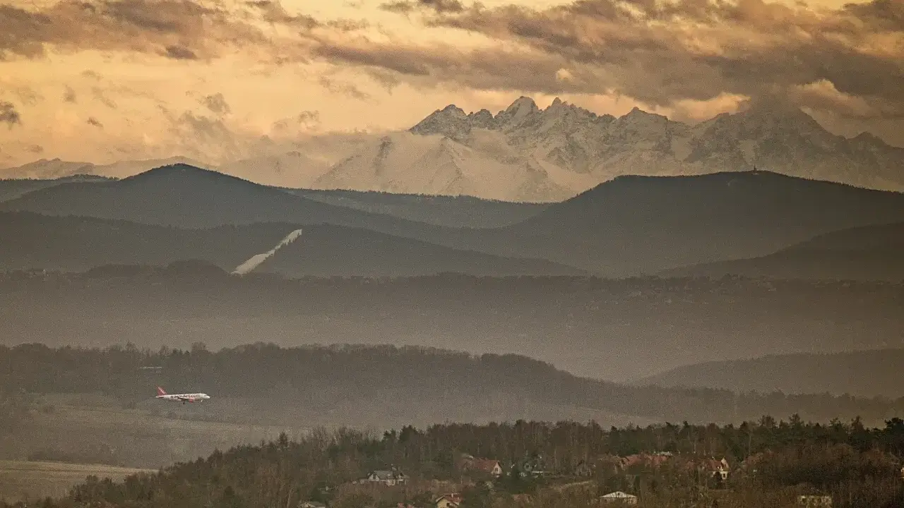 Widok na Tatry z Krakowa. Samolot leci nad mglistymi wzgórzami, a za nimi widać ośnieżone szczyty.