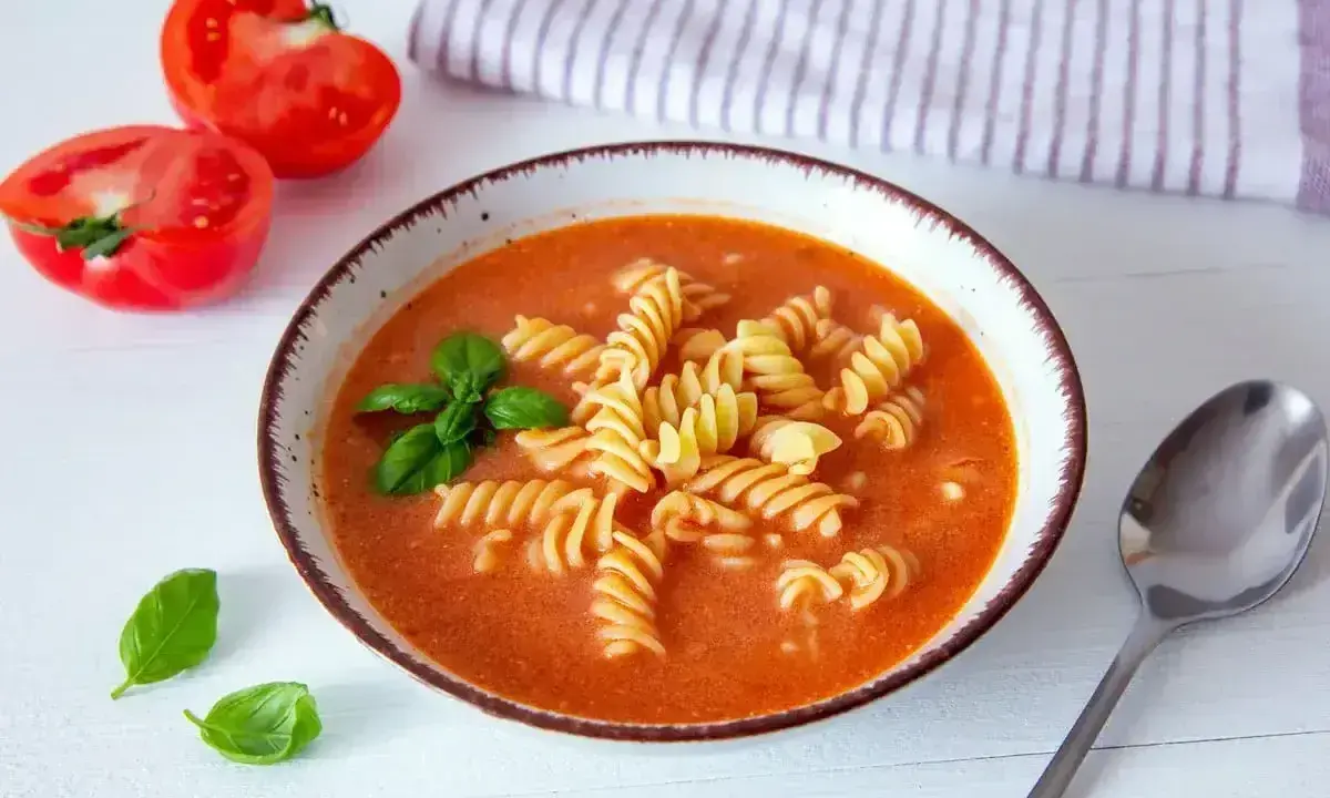 A miseczce zupy pomidorowej z makaronem fusilli, listkami bazylii i połówkami pomidorów obok. Idealne przyprawy do zupy pomidorowej.