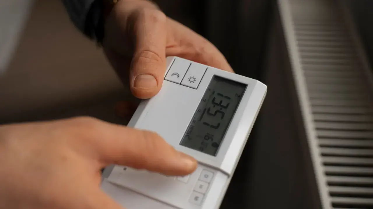 Dłoń naciska przycisk na białym sterowniku, by ustawić temperaturę na grzejniku.