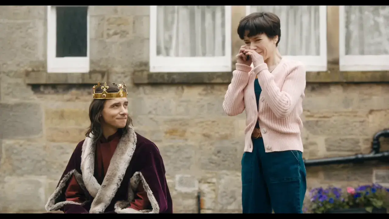 Un re con la corona e la pelliccia, forse il protagonista di "the lost king film", guarda una donna che ride con le mani sul viso.