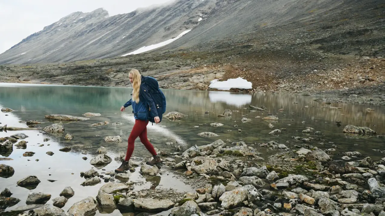 Kobieta z plecakiem przemierza kamieniste brzegi górskiego jeziora. W tle skaliste zbocza, idealne dla skandynawskie marki outdoorowe.