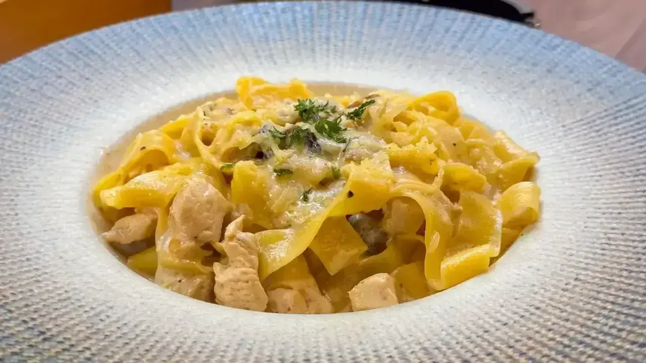 Pyszny makaron włoski z kawałkami kurczaka w kremowym sosie, posypany ziołami i parmezanem.