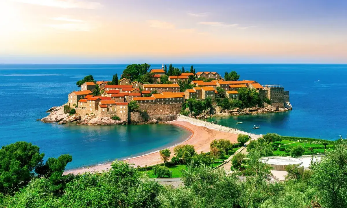 Drömresa till Montenegro: en pittoresk ö med stenhus och röda tak, omgiven av turkost hav. Perfekt för en solsemester.