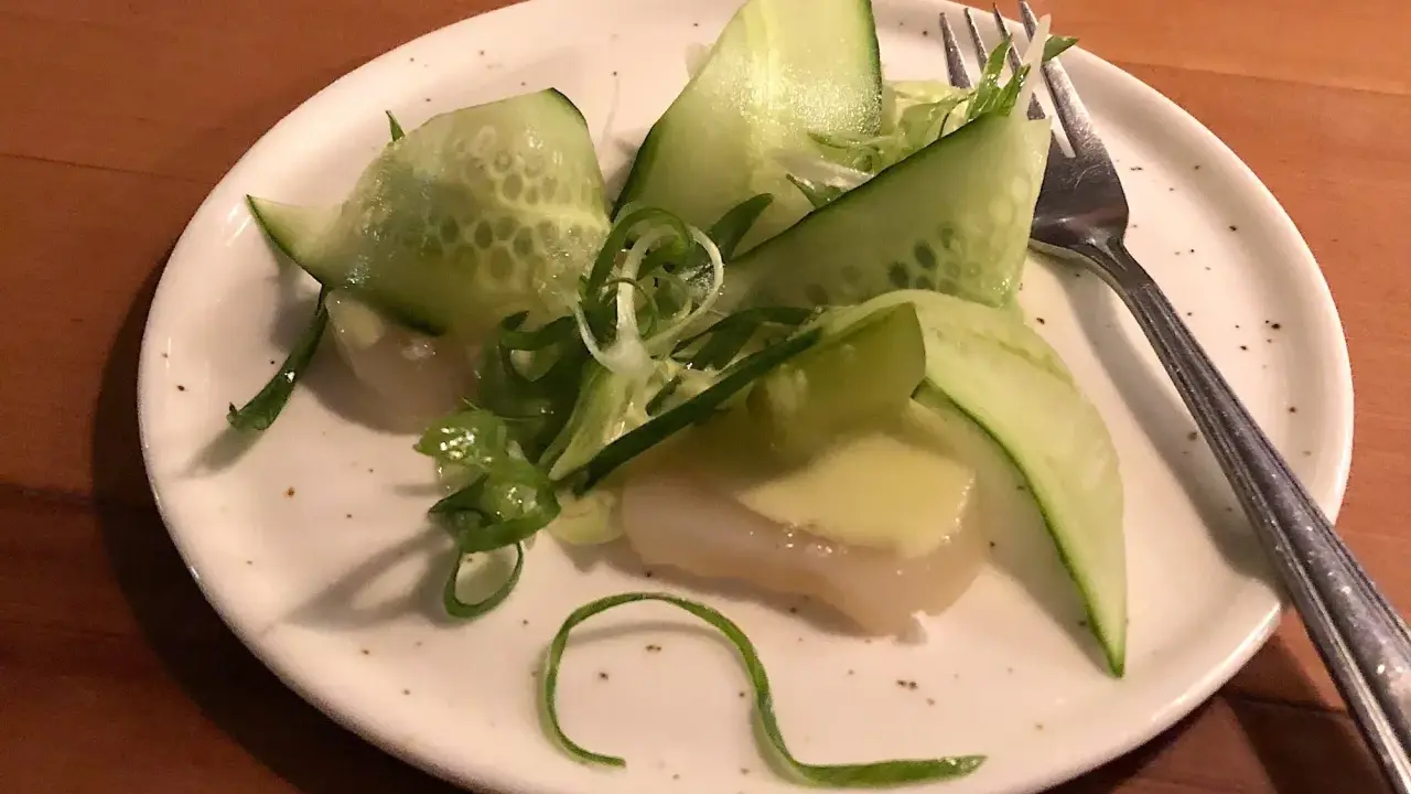 En läcker pilgrimsmussla med gurka och salladslök, serverad på en tallrik i en mysig wood restaurang.