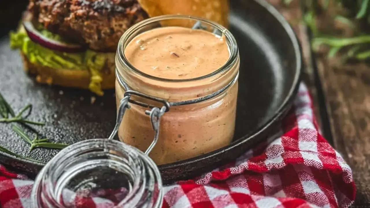 Leckere, cremige Sauce im Glas, perfekt zum schnelle Burger Sauce selber machen. Dazu ein saftiger Burger auf einem Gusseisen-Teller.
