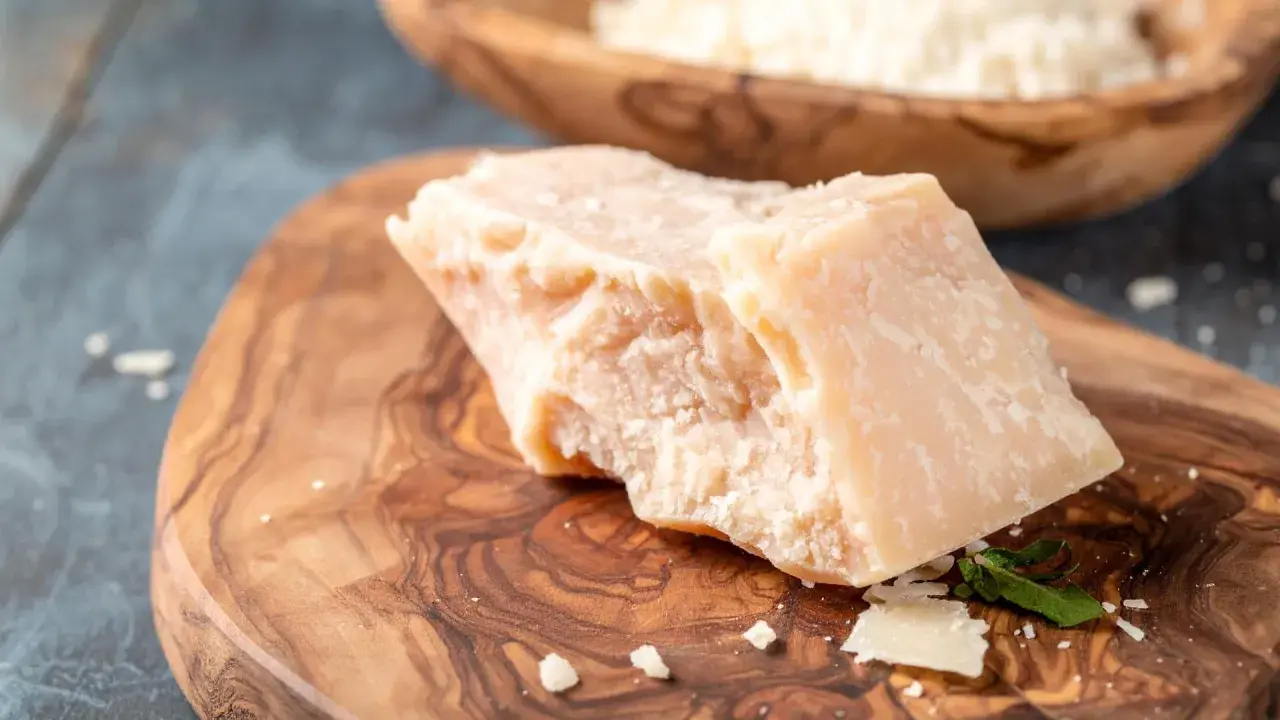 Kawałek twardego sera, przypominającego Grana Padano i parmezan, leży na drewnianej desce.