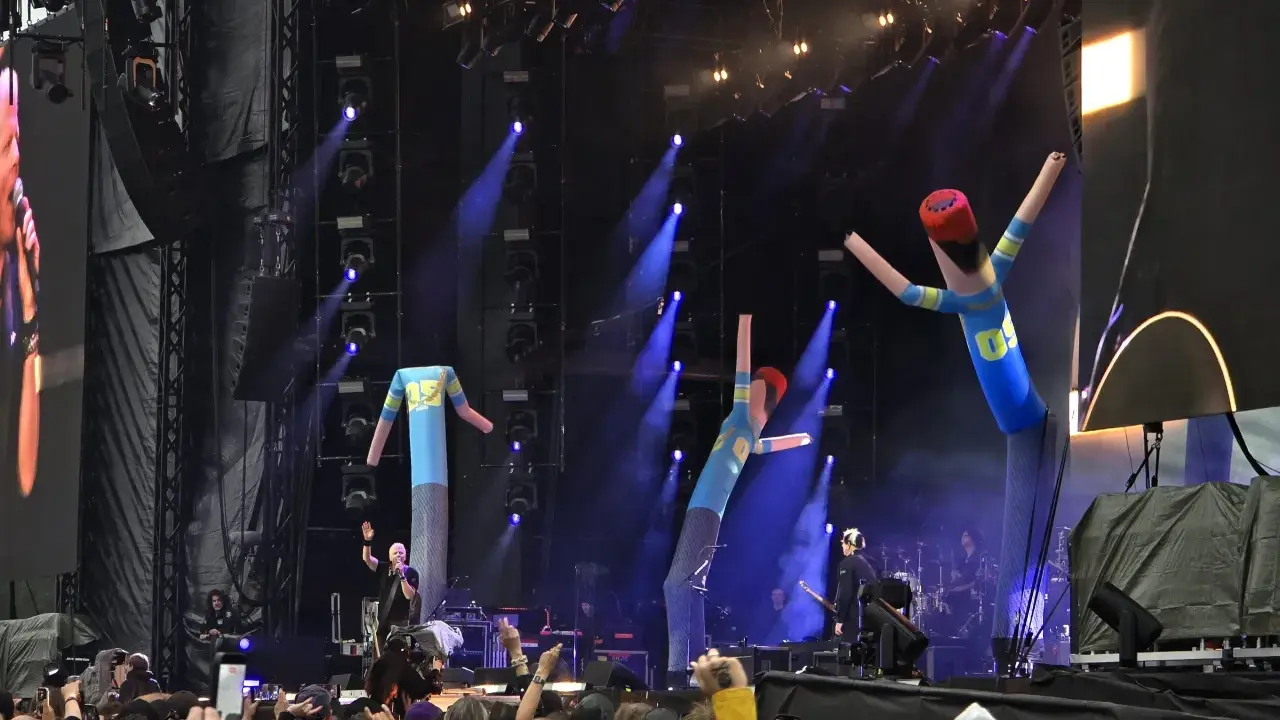 The Offspring Sverige spelar live med uppblåsbara figurer på scenen. Blå ljus och rök skapar en festlig stämning.